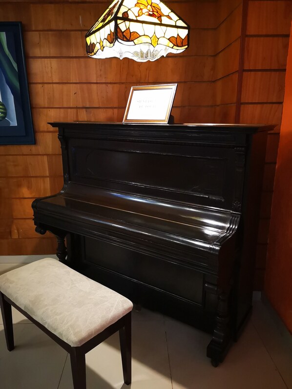 Um piano preto com um banquinho à frente, um certificado emoldurado em cima e uma luminária de vitrais acima.