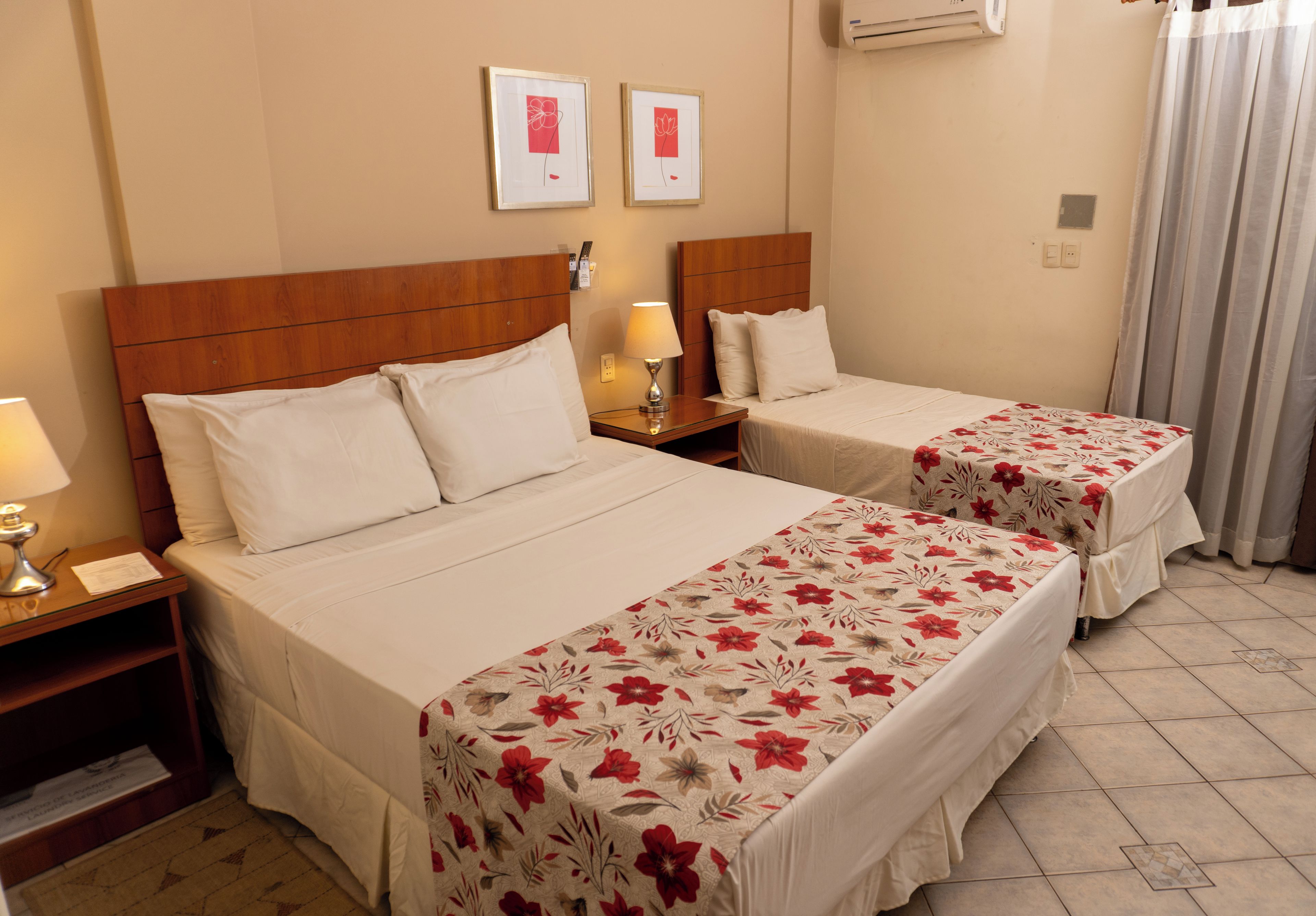 Une chambre d’hôtel avec deux lits, une tête de lit en bois, une table de chevet avec une lampe et un climatiseur fixé au mur.