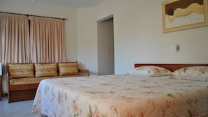 A bedroom with a large bed, a wooden bench with cushions, and a painting on the wall. - Residencial Sol e Mar de Floripa (Florianópolis)