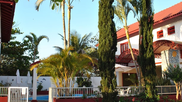 A building with a red roof and white walls, surrounded by palm trees and a gravel driveway. - Residencial Sol e Mar de Floripa (Florianópolis)