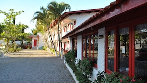 A building with a red roof and white walls, featuring large windows and a gravel pathway. - Residencial Sol e Mar de Floripa (Florianópolis)