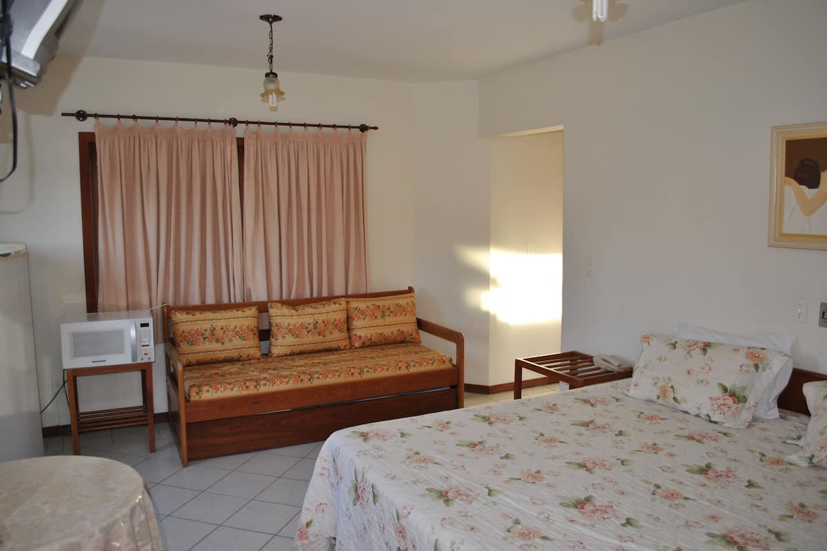 A bedroom with a bed, a sofa, a bedside table, a lamp, and a window with curtains.