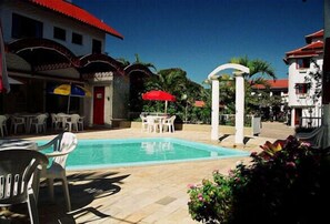 Un área de piscina con sillones de descanso y sombrillas, rodeada de edificios con tejados rojos.