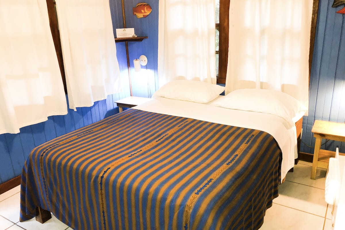 Una cama con una colcha a rayas, una mesita de noche y un estante en la pared con un objeto decorativo.