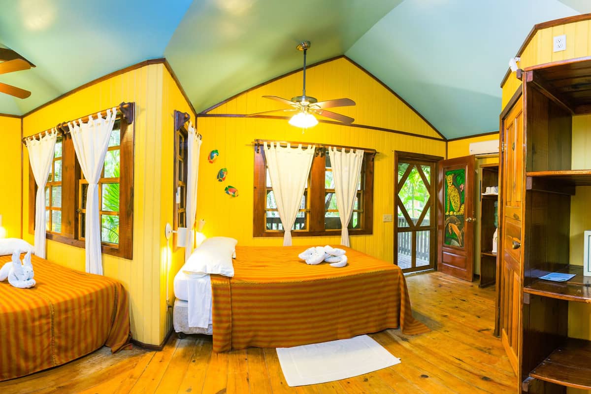 Habitación con dos camas, piso de madera, ventiladores de techo y ventanas grandes con cortinas.