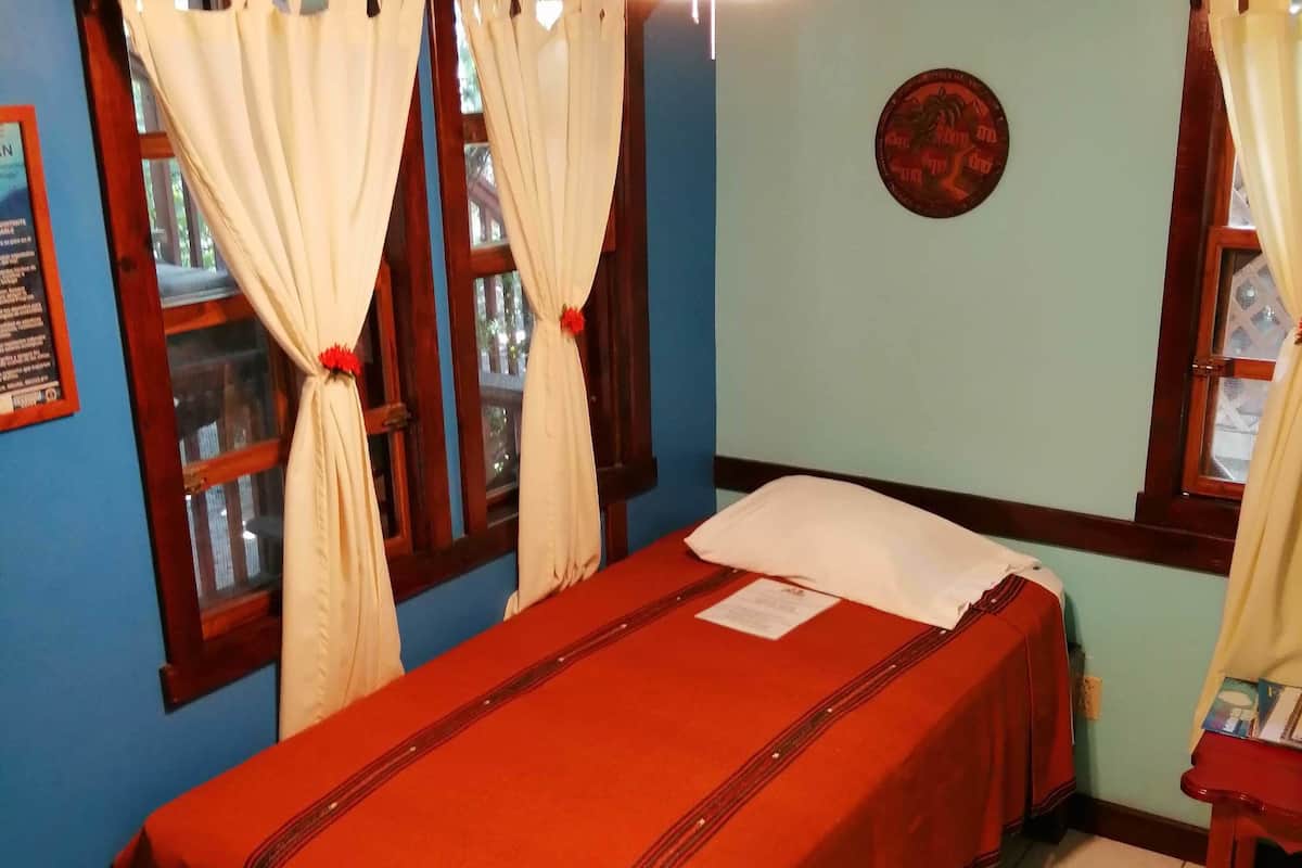 Una habitación con cama, cortinas, ventilador de techo y un panel en la pared.