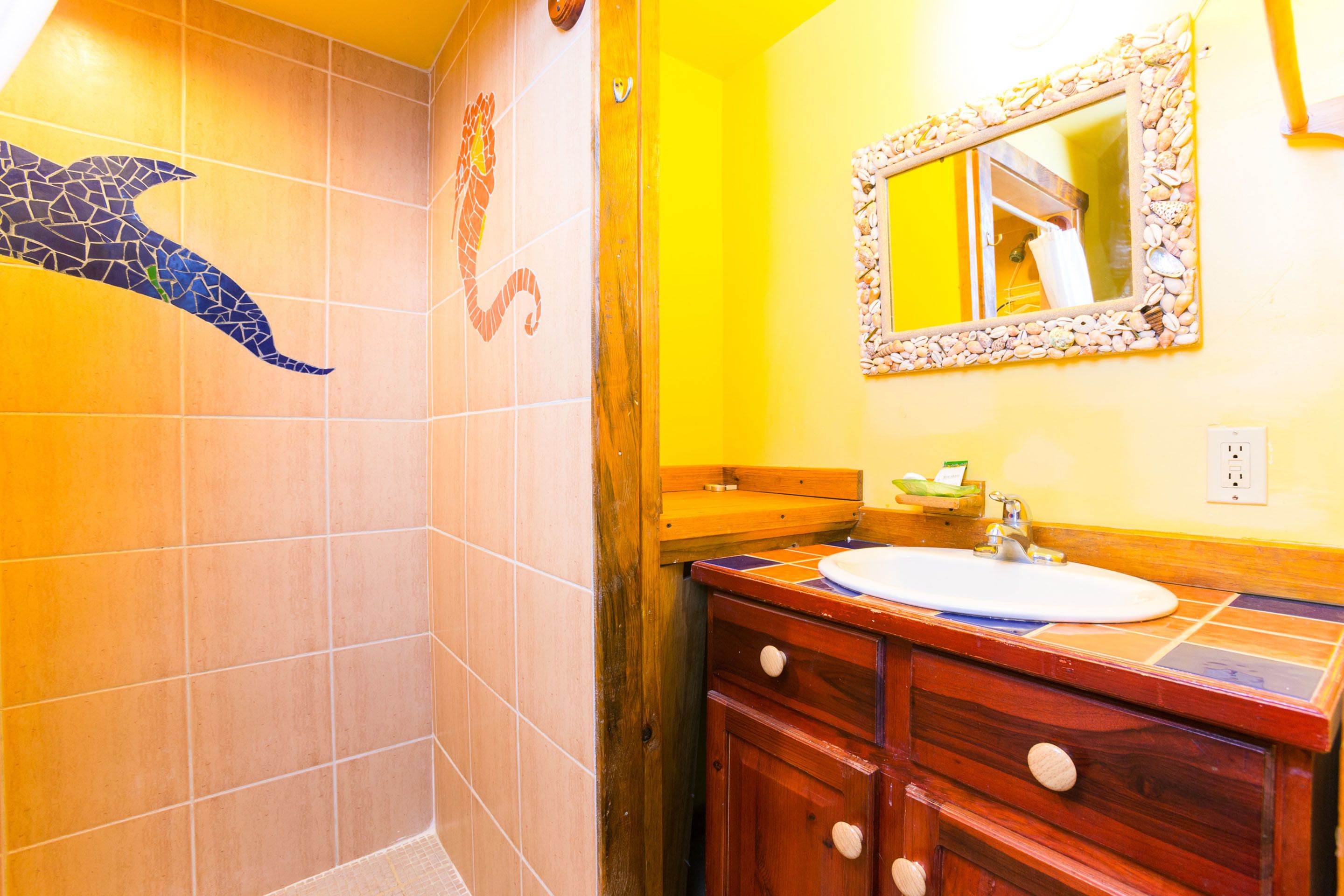 A bathroom with a tiled shower area, a wooden vanity with a sink, and a mirror with a decorative frame.
