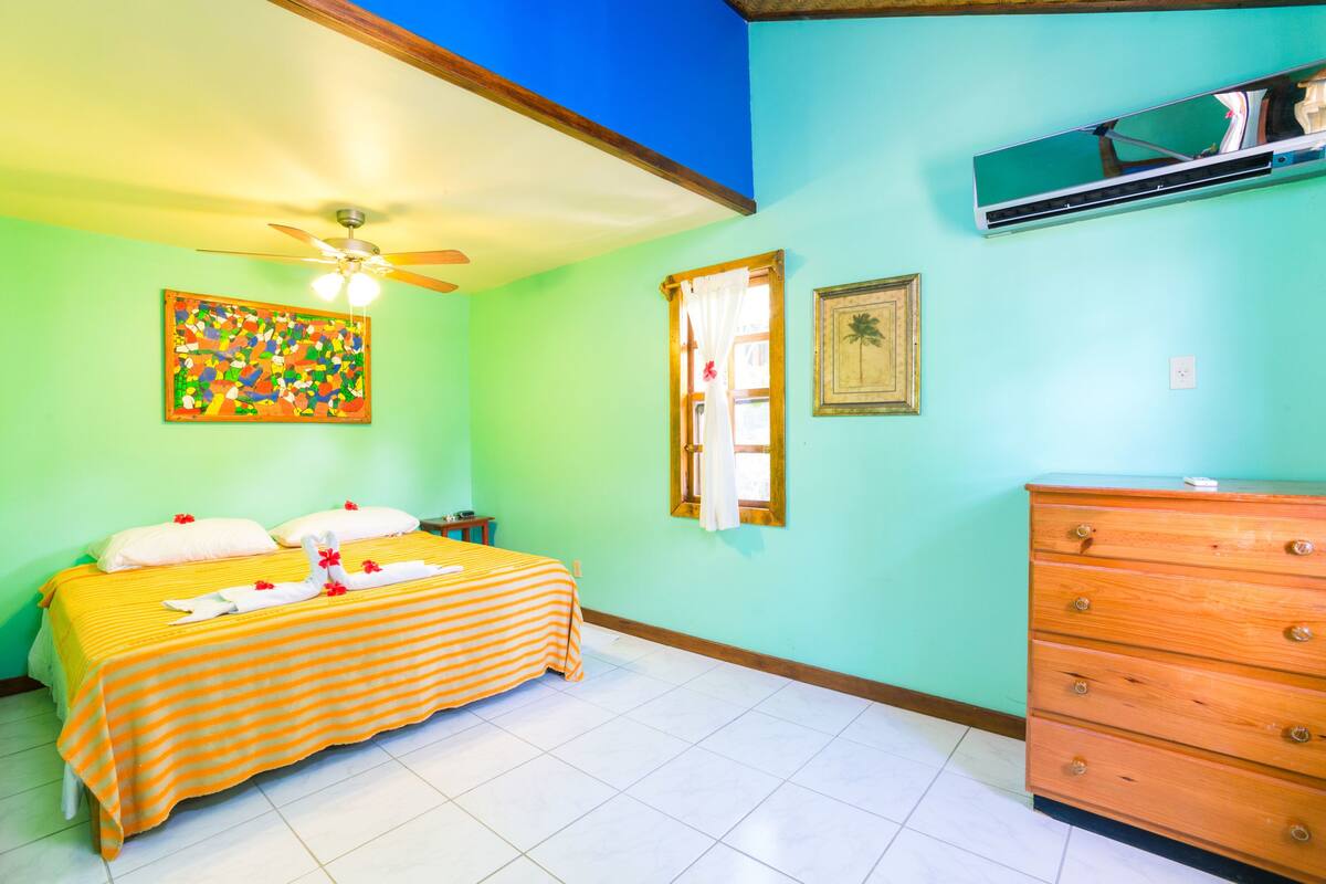 Una habitación con una cama, un aparador, un ventilador de techo y un cuadro en la pared.