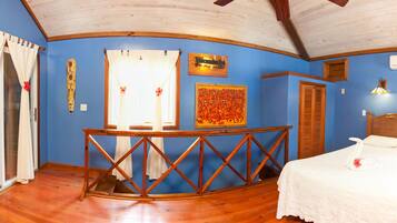 Una habitación con una cama, una mesa de madera, un armario pequeño y un ventanal con cortinas.