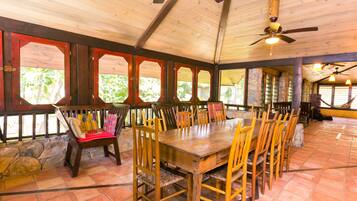 A spacious dining area with a large wooden table and chairs, stone walls, and a high ceiling with wooden beams.