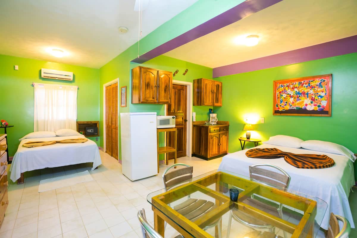 Una habitación con dos camas, una kitchenette, una mesa de comedor y un cuadro colorido en la pared.