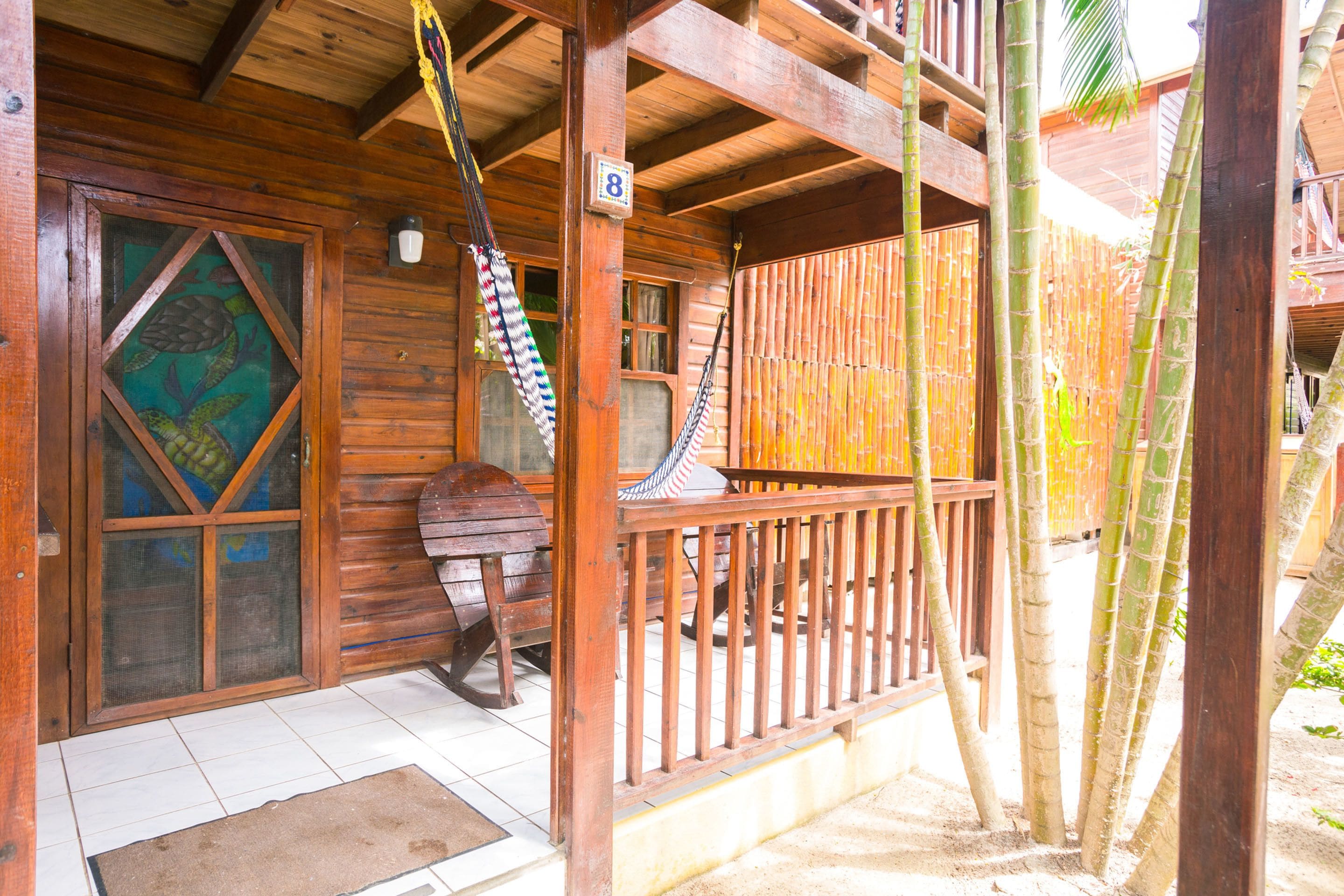 Una cabaña de madera con un balcón, una puerta con un celosía decorativa y una hamaca colgada en la pared.