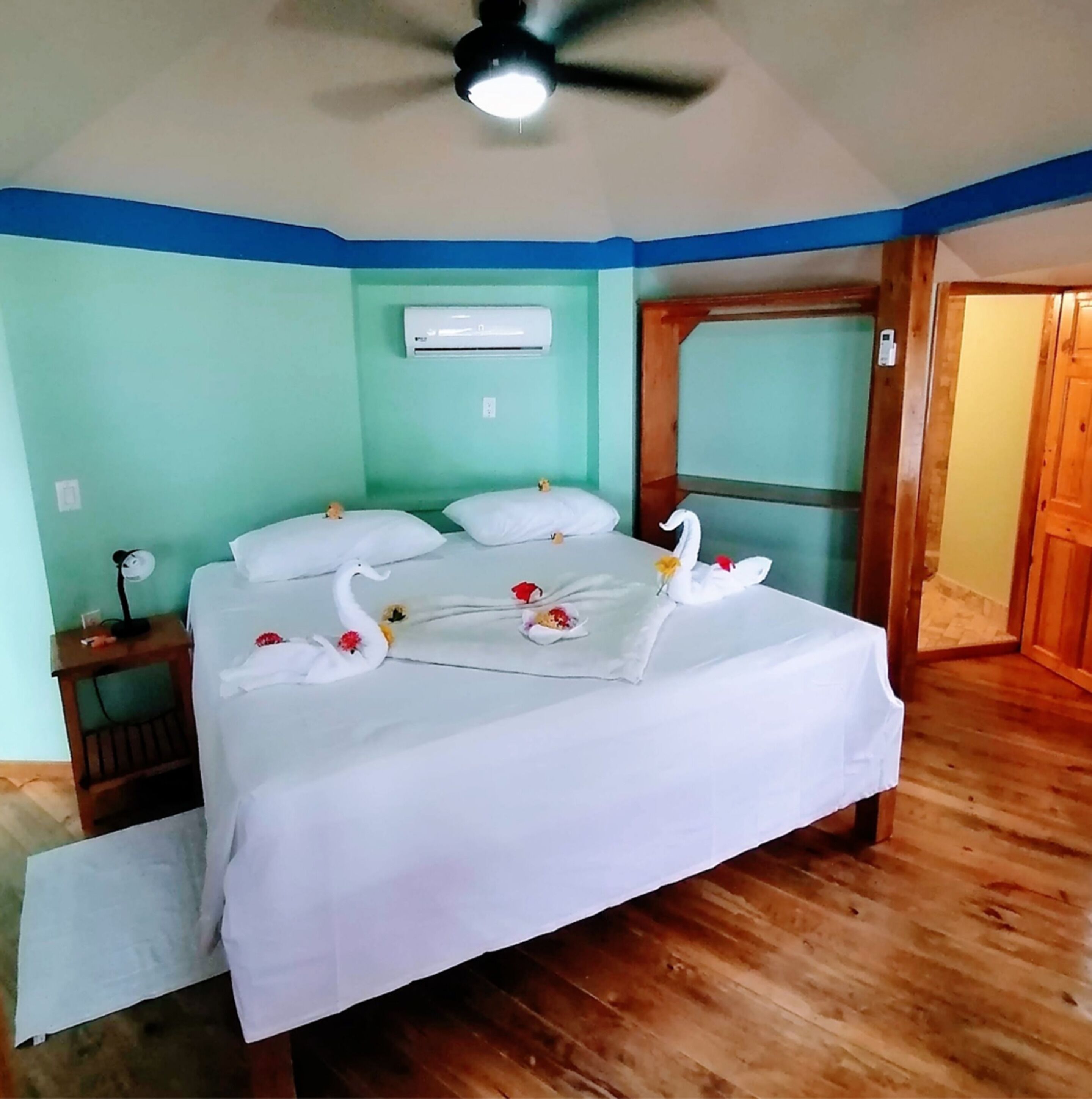Een slaapkamer met een bed, een plafondventilator, een airconditioner en een houten deur.