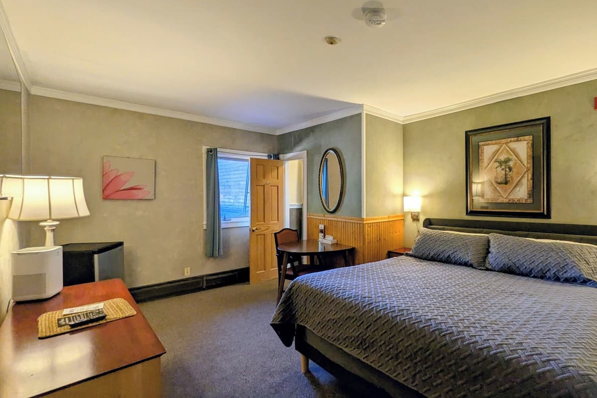 A hotel room with a bed, bedside tables, a desk, a chair, a lamp, a mirror, and artwork on the walls.