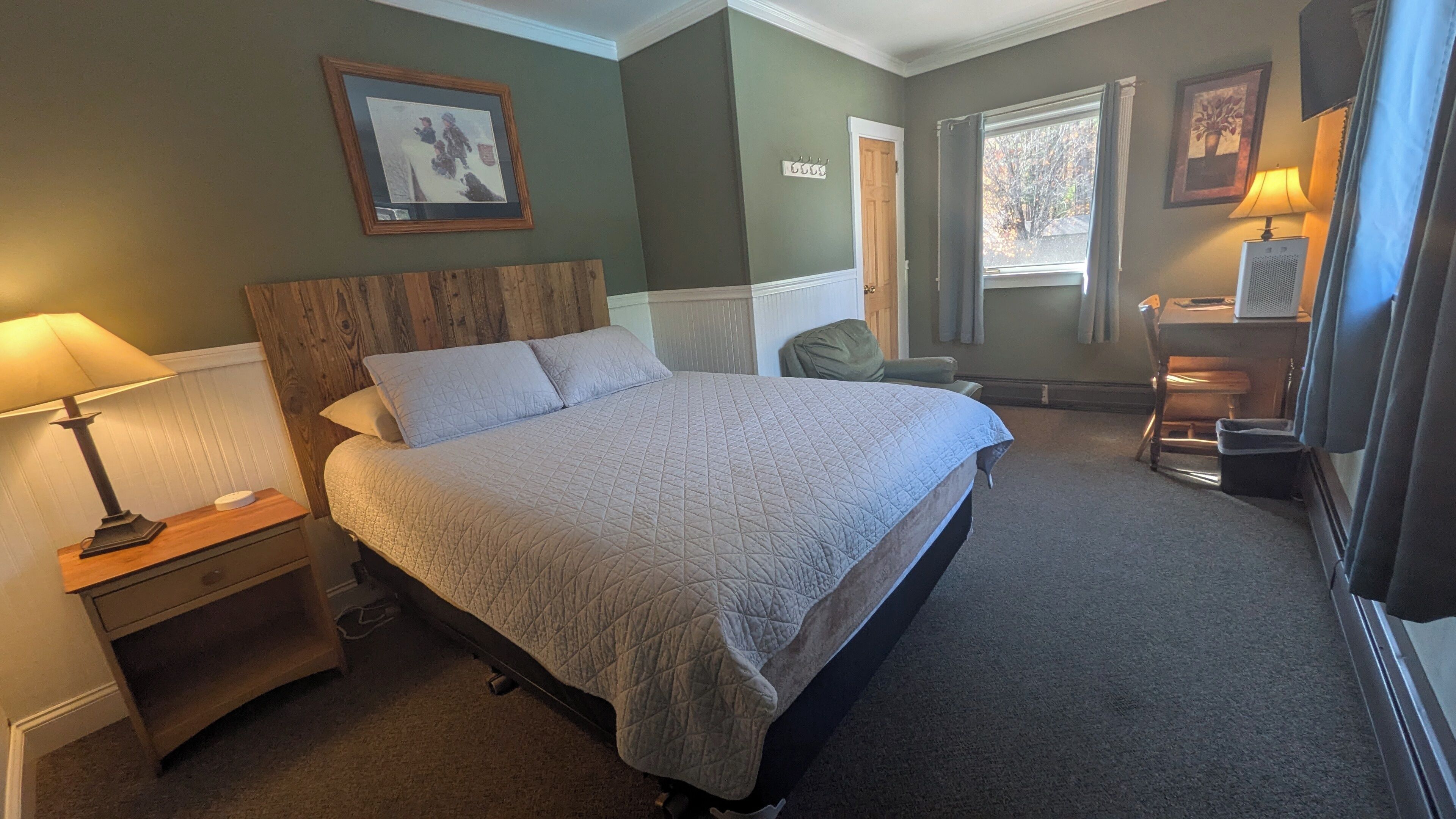 A neatly arranged bedroom with a large bed, a bedside table with a lamp, a chair, and a desk with a lamp.