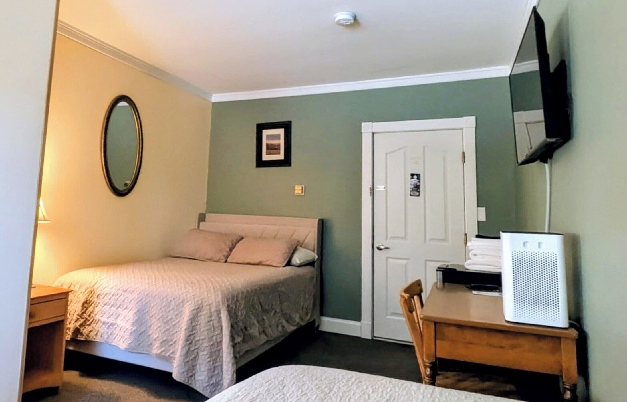 A bedroom with a bed, a desk, a chair, a mirror, and a door.