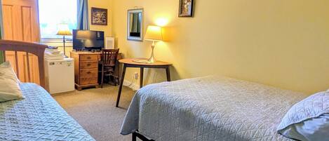 A bedroom with two beds, a desk with a chair, a television, and a lamp.