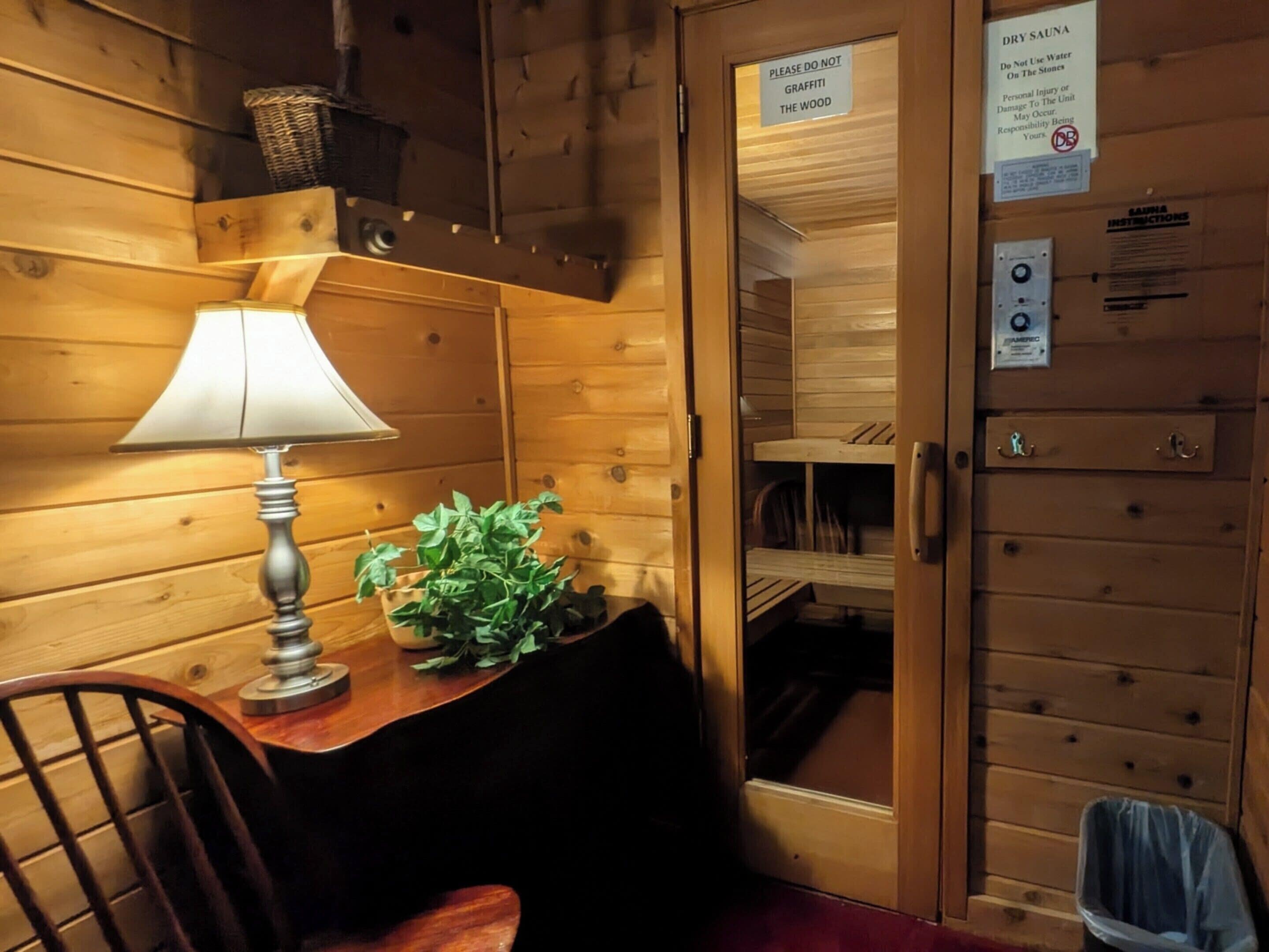 A wooden cabin interior with a table, a lamp, a plant, and a door with a sign.