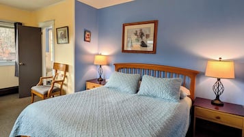 A bedroom with a large bed, two bedside tables with lamps, a chair, and a door.