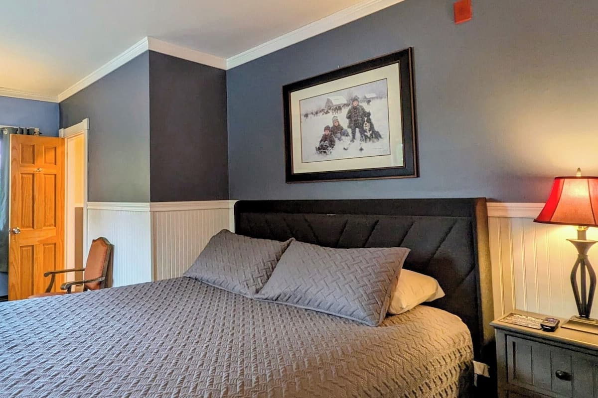 A bedroom with a bed, a nightstand, a lamp, a framed picture on the wall, and a door.
