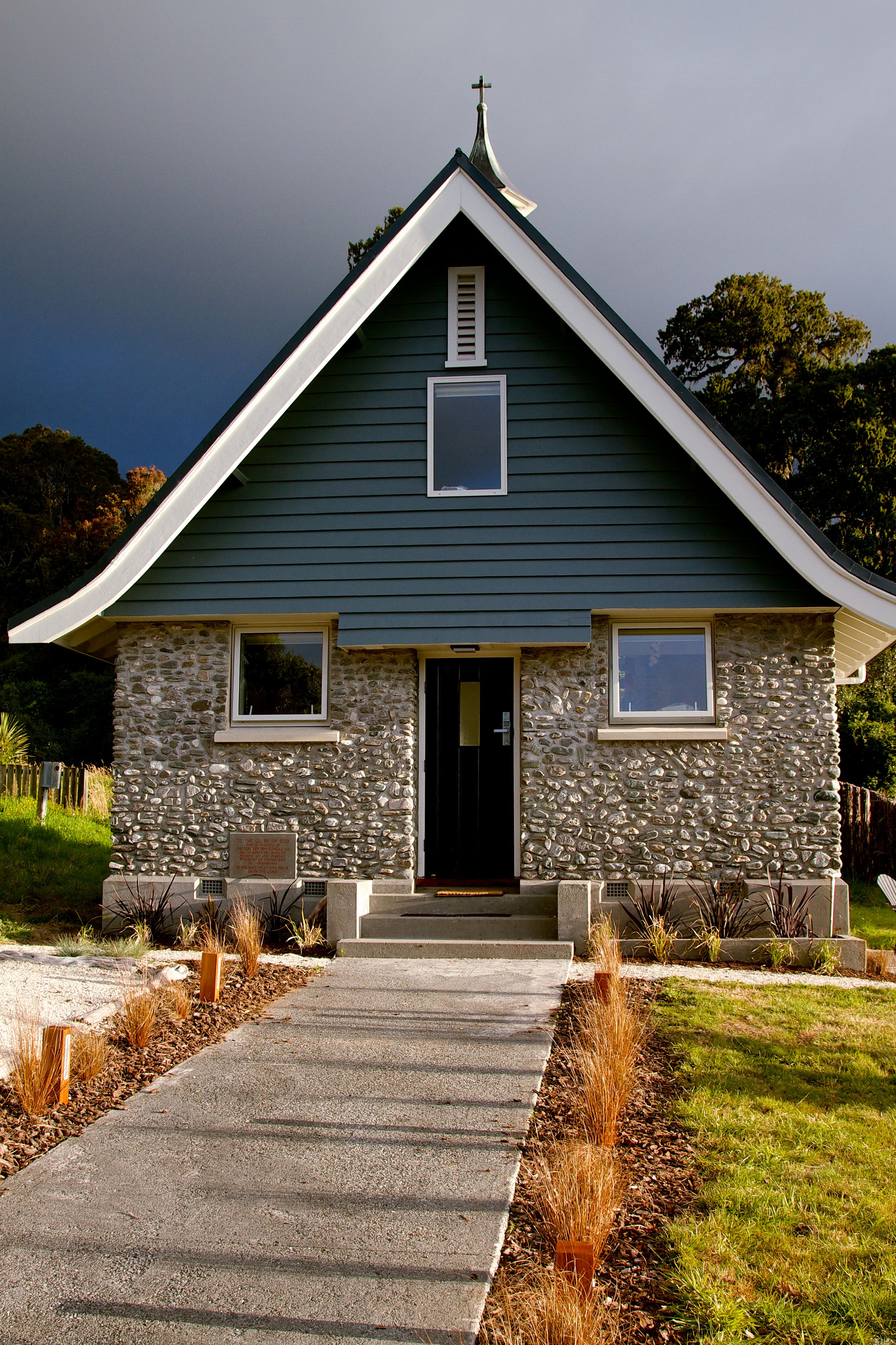 A church with a stone facade, a black door, and a small porch with two chairs.