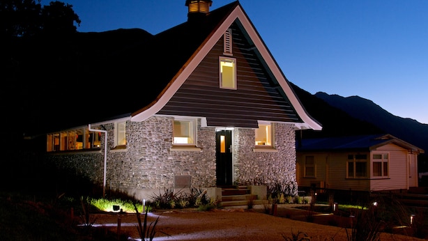 Una casa de piedra con un techo empinado a dos aguas, una pequeña torre de campanas y una entrada bien iluminada.