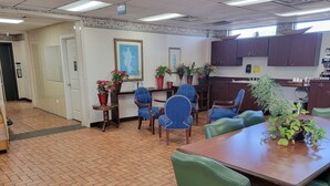 A dining area with a brick floor, wooden tables, and chairs. There are potted plants on the tables and a framed picture on the wall.