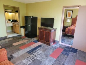 Habitación de hotel con kitchenette, un televisor sobre un mueble de madera, una alfombra estampada y una cama con colcha estampada.