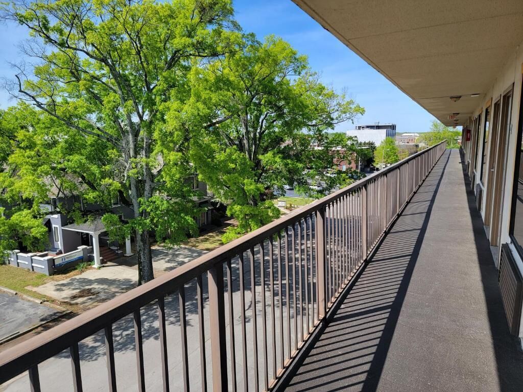 A covered outdoor corridor with a metal railing, trees, and a building in the background.