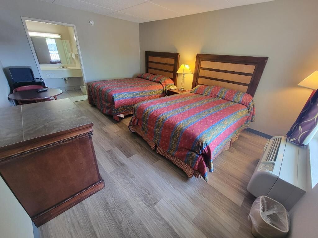 A hotel room with two beds, a desk, a chair, a mirror, and a waste bin.