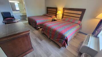A hotel room with two beds, a desk, a chair, a mirror, and a waste bin.