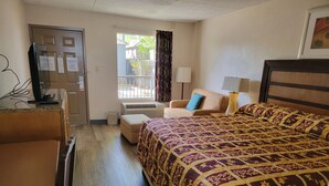 A hotel room with a bed, a chair, a desk, a television, and a window with curtains.
