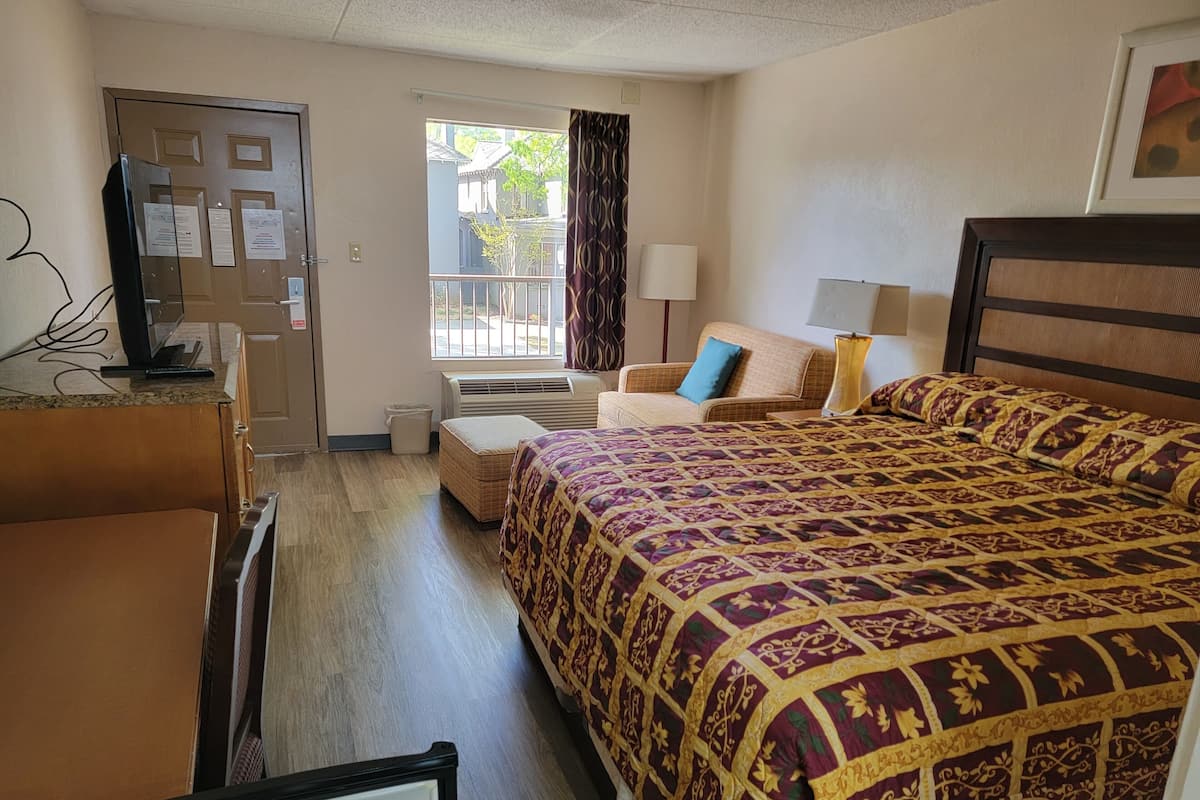 Ein Hotelzimmer mit Bett, Sessel, Schreibtisch, Fernseher und einem Fenster mit Vorhängen.