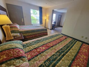 Una habitación de hotel con dos camas, un escritorio, una silla y un ventanal con cortinas.