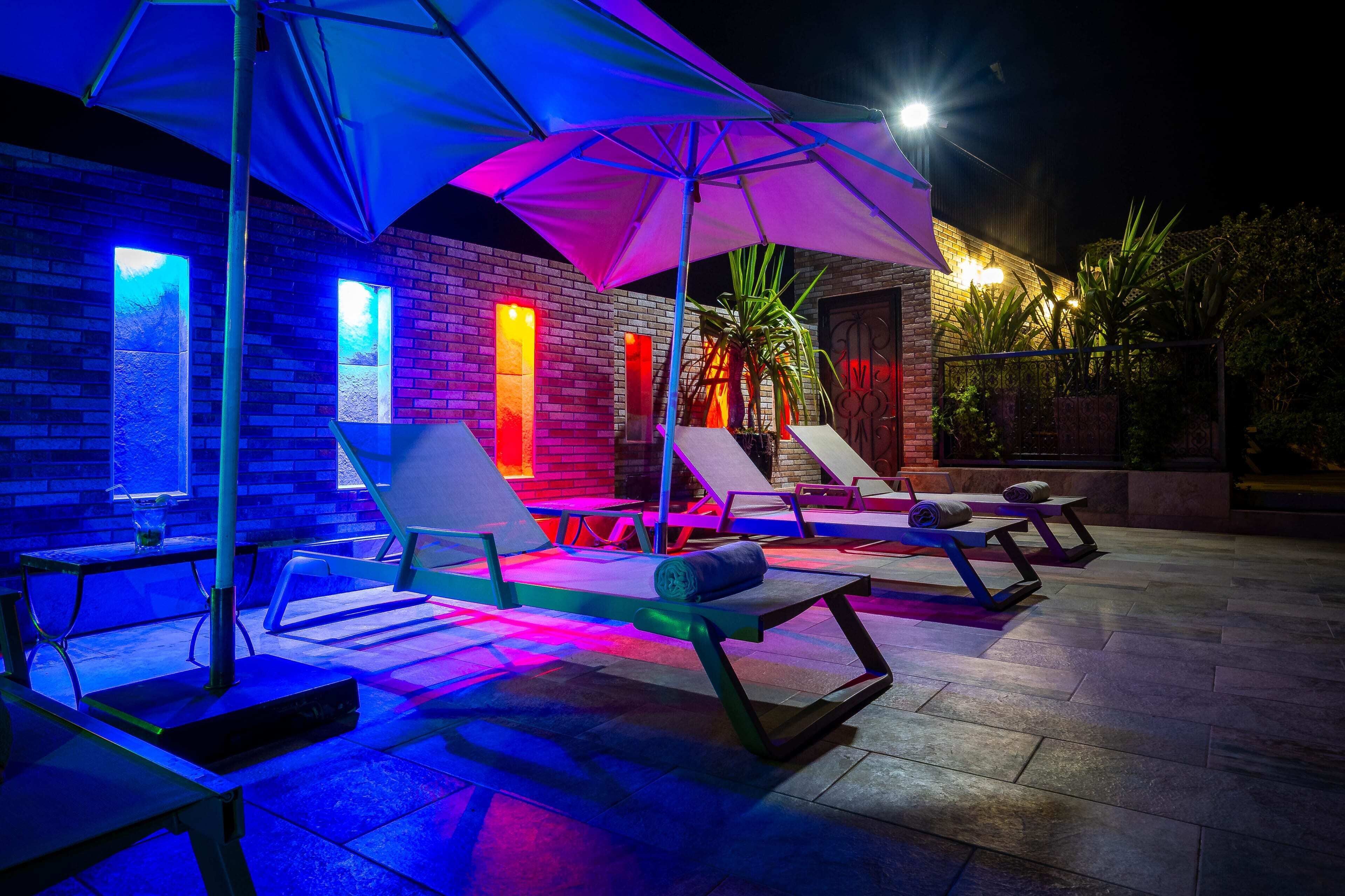An outdoor lounge area with seating and umbrellas, a brick wall, and a well-lit building in the background.