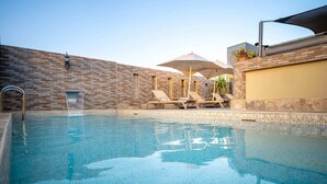 Una piscina con sillones de playa y sombrillas, un muro de ladrillo y una barandilla metálica.