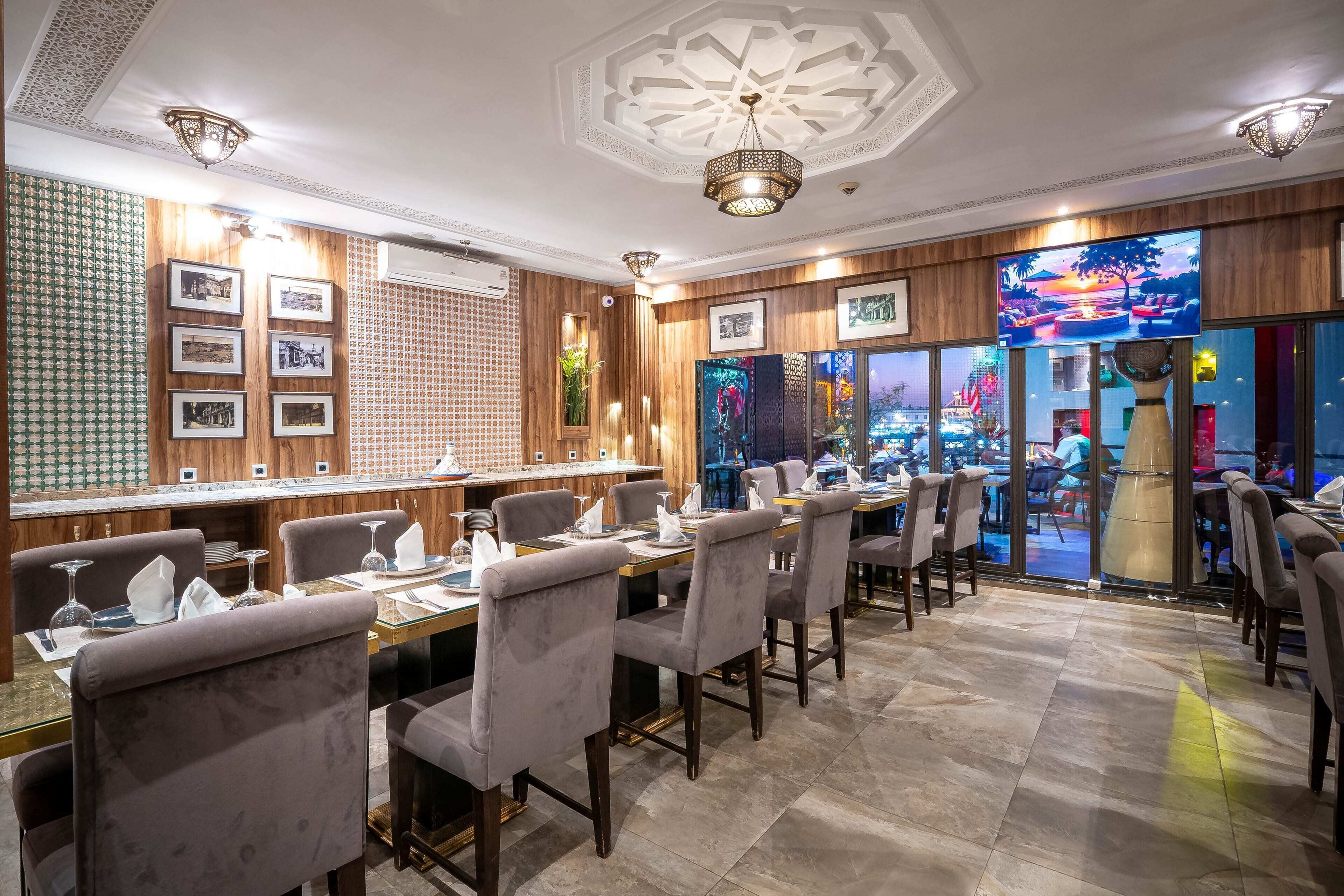 A restaurant with a long table, chairs, framed pictures, and a TV screen.