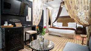 Una habitación con cama, un escritorio con un florero, un espejo y cortinas estampadas.