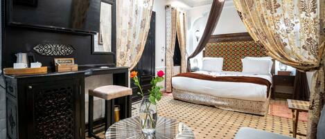 A room with a bed, a desk with a vase, a mirror, and patterned curtains.