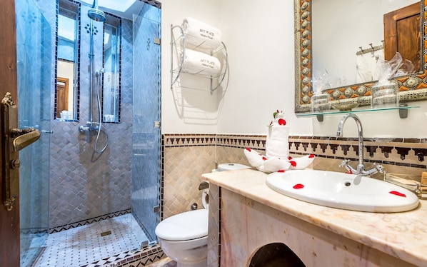 Un baño con ducha de vidrio, inodoro, lavamanos con encimera de mármol y espejo con marco decorativo.