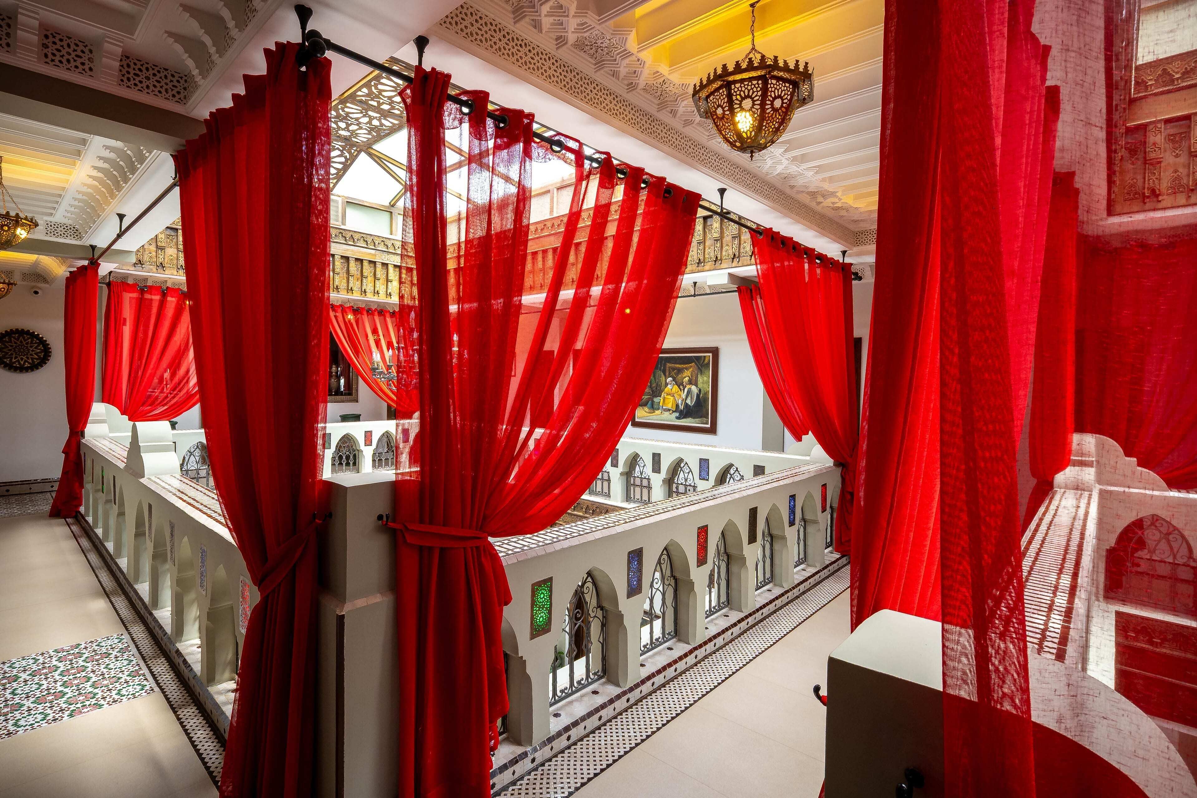 A corridor with red curtains, a chandelier, and a view of a building with arches.