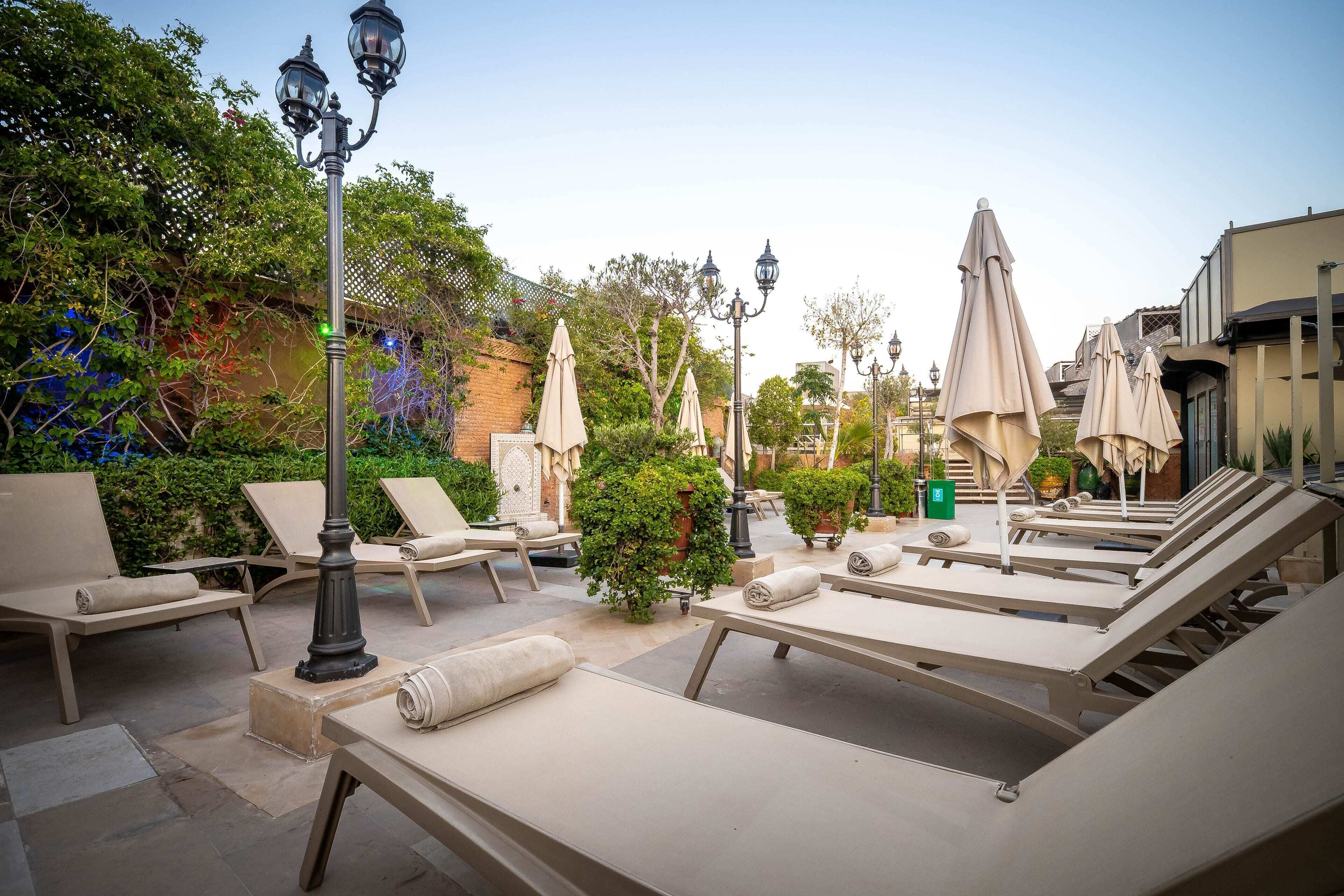 A sunlit outdoor lounge area with lounge chairs, umbrellas, and decorative street lamps.