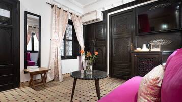 A room with a patterned floor, a round glass table with a vase of flowers, a pink sofa, and dark wooden doors with intricate designs.