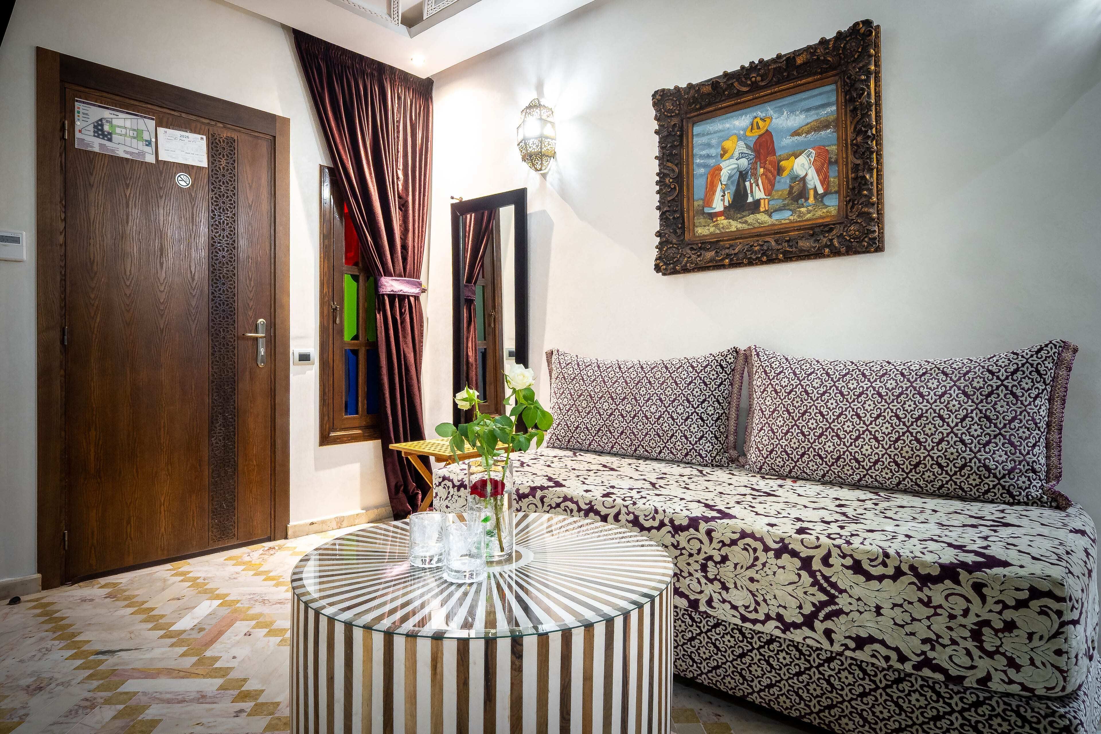 A room with a patterned sofa, a round table with a vase, a framed picture on the wall, and a door with a sign.