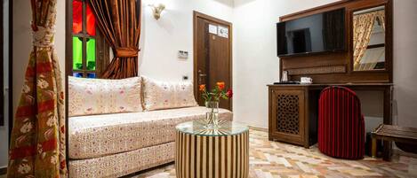 A living room with a sofa, a round table, a television, and a patterned floor.