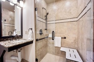 Un baño moderno con cabina de ducha de vidrio, lavamanos con encimera de granito y un espejo grande.