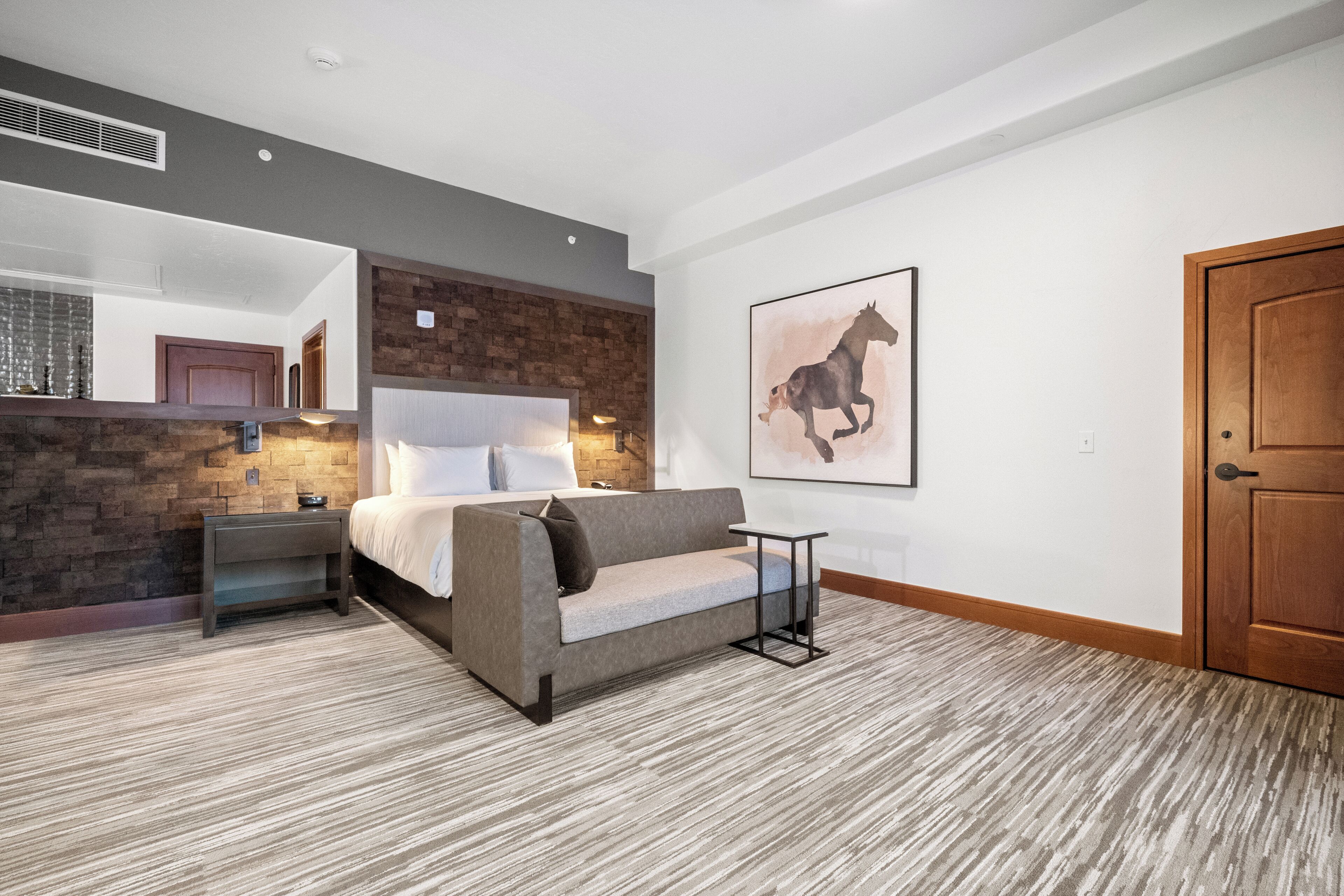 A bedroom with a bed, a sofa, a small table, a wooden door, and a brick wall.