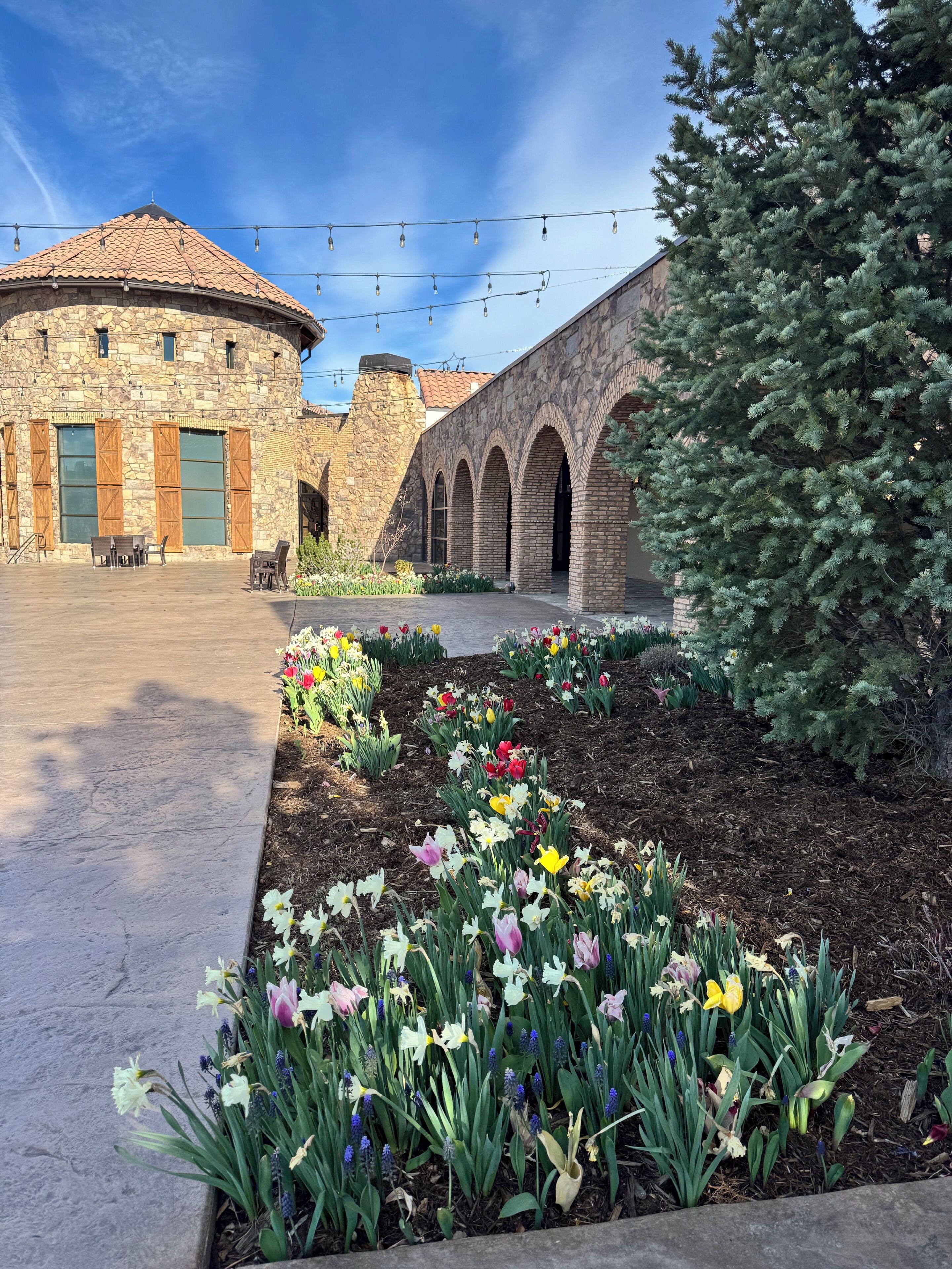 Ein Innenhof mit einem Steinhaus, gewölbten Gängen und einer Vielzahl von Blumen.