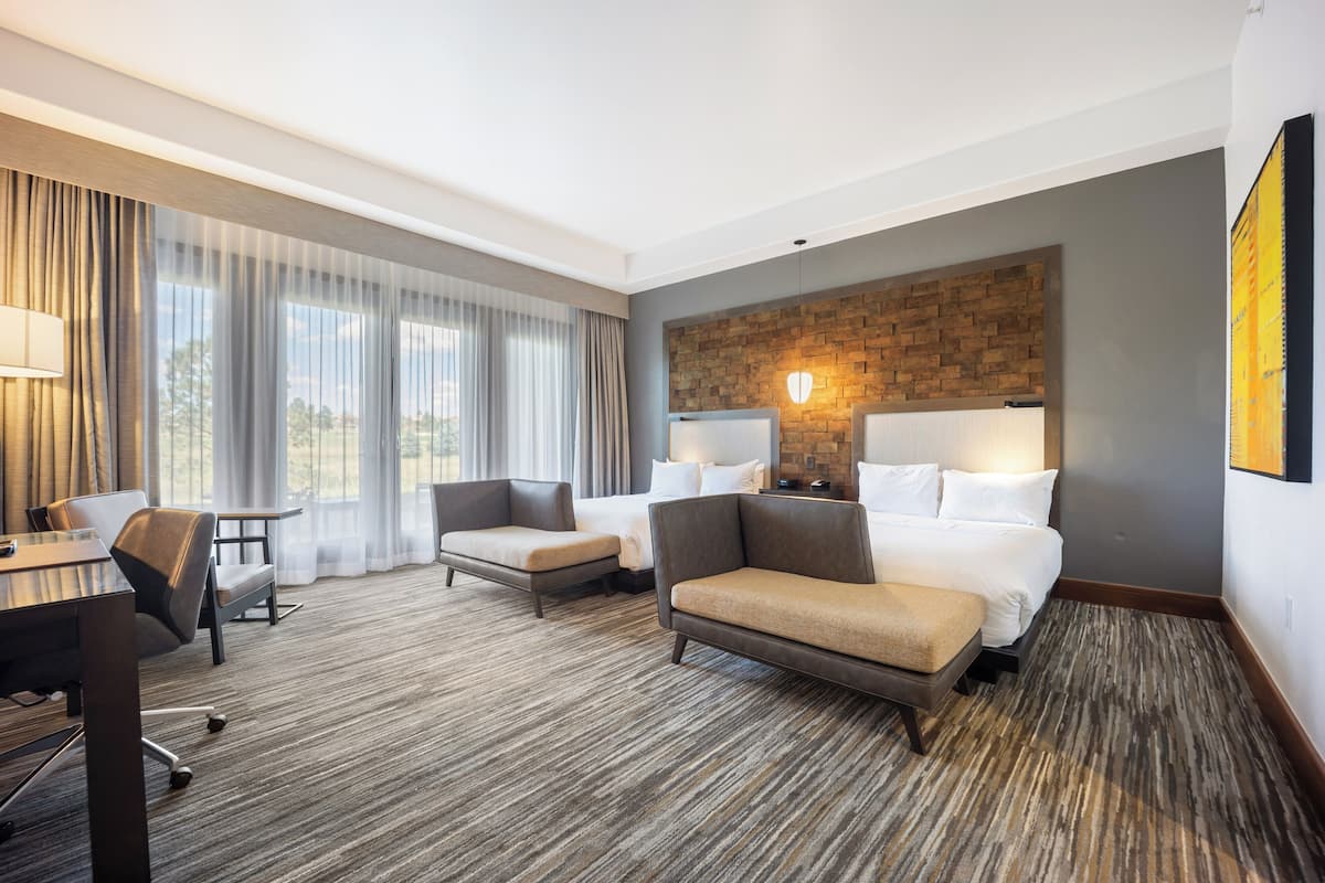 Een hotelkamer met een groot bed, twee fauteuils, een bureau en uitzicht op de omgeving.
