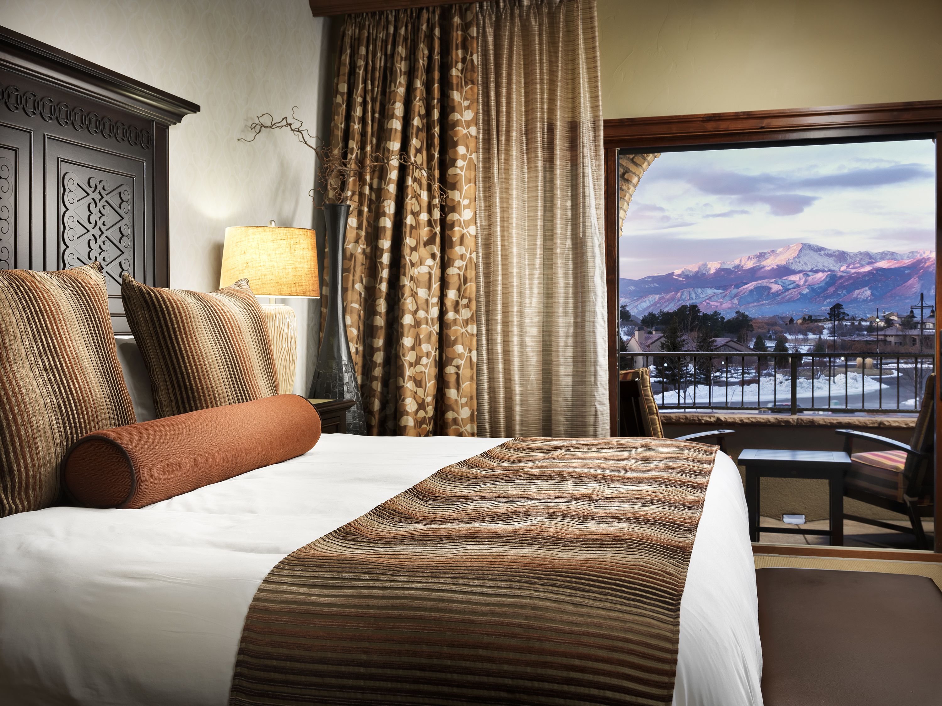 A hotel room with a large bed, a view of mountains, and a balcony with a table and chairs.